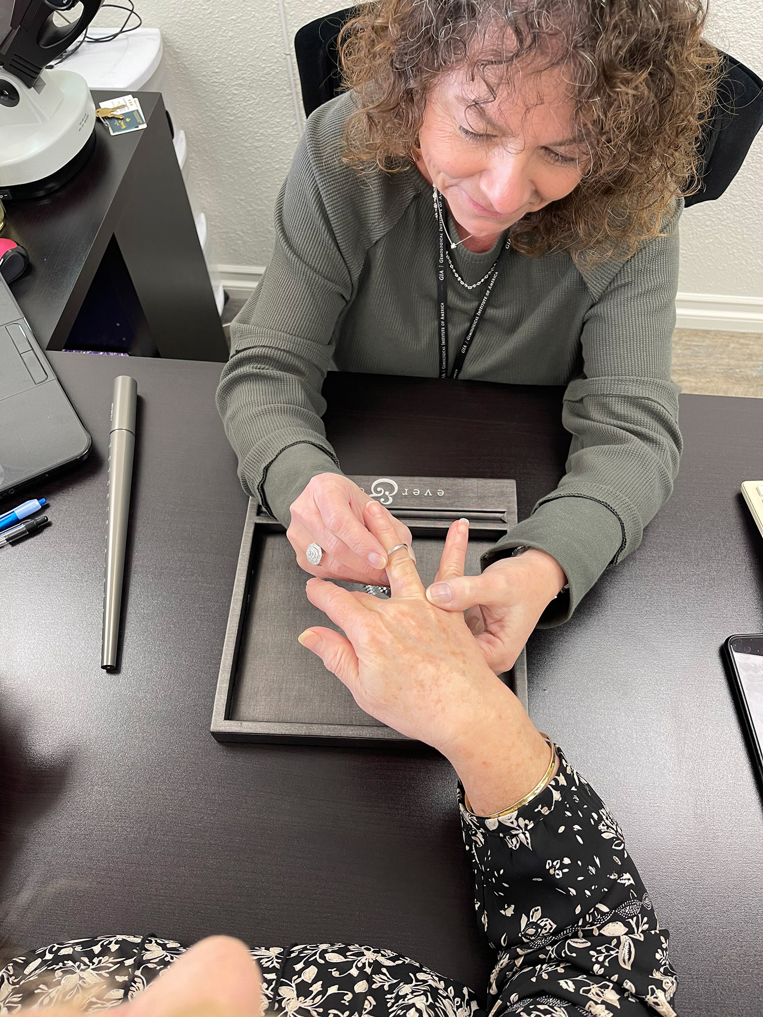 Woman in a sage green long sleeve shirt inspecting a ring on another woman's finger