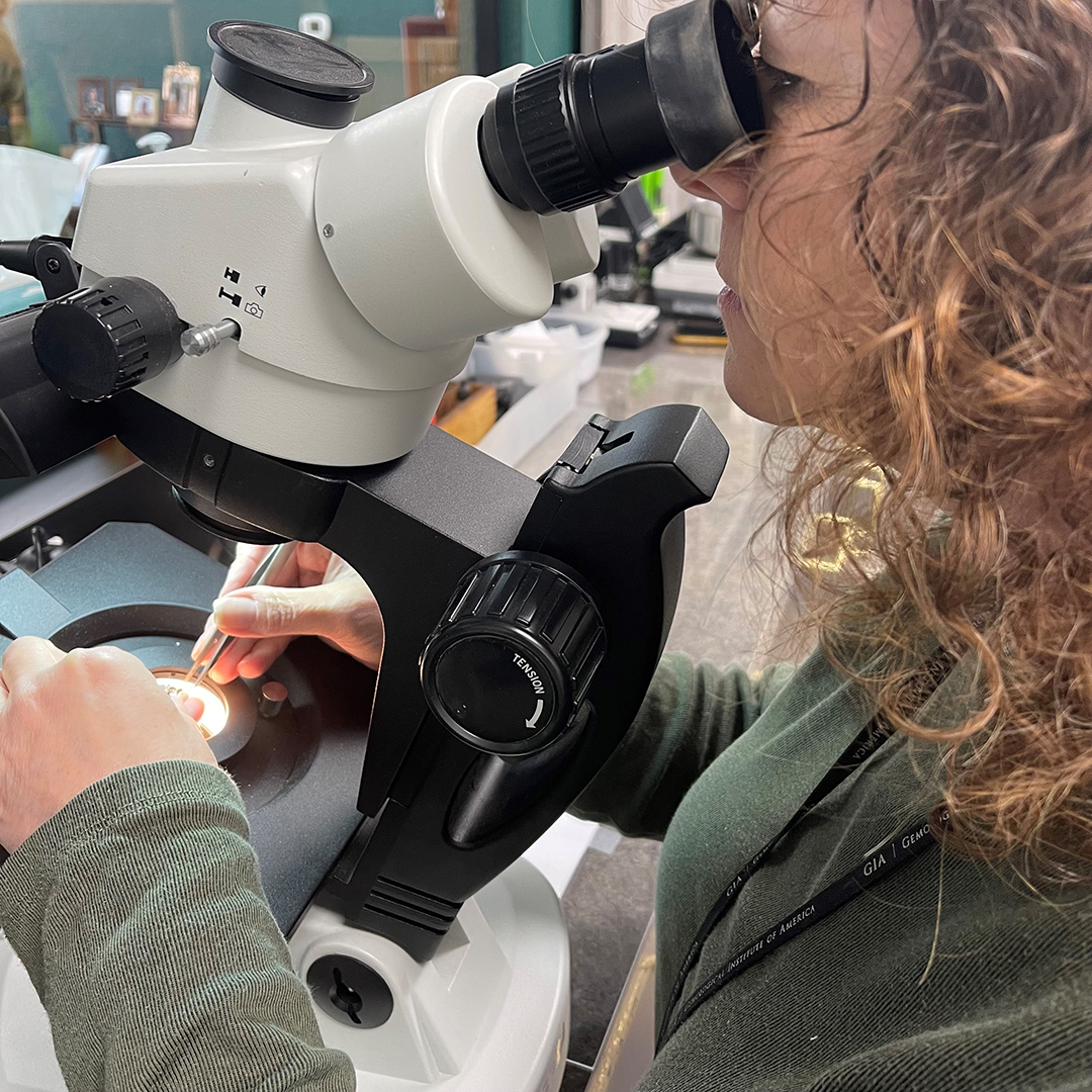 A woman analyzing a piece of jewelry under a microscope